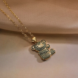 Detailed view of gold bear pendant with green and black zircons on brown satin background