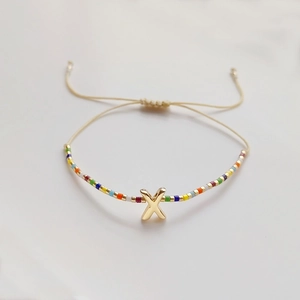 Detail eines bunten Miyuki-Perlenarmbands mit goldenem Buchstaben X und verstellbarer Kordel