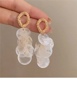 Close-up of golden textured stud earrings with white shell tassel sequins detail