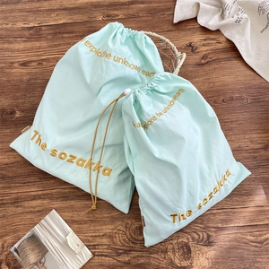 Detail of mint green drawstring storage bags with yellow embroidery on dark wood floor