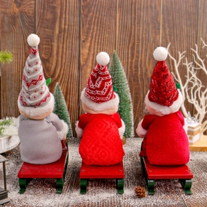 Three Christmas gnomes on a red metal sled with snow-covered trees and pine cones