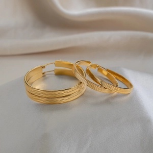 Macro detail of gold-plated snake chain texture hoop earrings on luxury satin cloth