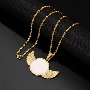 Golden iced-out angel wing photo pendant necklace with sparkling crystals on black surface