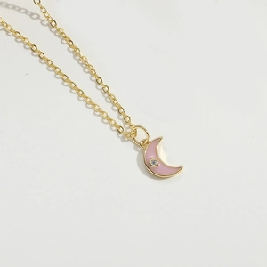 Macro detail of golden chain necklace featuring a pink crescent moon pendant with zircon