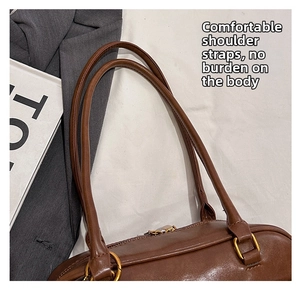Detail of smooth dark brown leather handle and gold metal hardware on Boston bag
