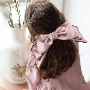 Close-up of a large pink satin bow hair clip styled on a girl's brown hair ponytail