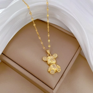 Macro detail of gold-plated bear pendant with pavé crystals on white silk background