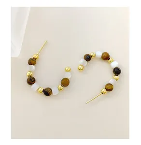 Macro detail of C-shaped earrings with brown tiger eye beads and gold metallic accents