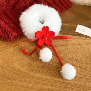 Detail of plush white faux fur hair tie with red flower and decorative mini pom-poms
