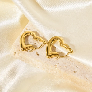 Dettaglio di orecchini a cerchio a cuore in oro 18K su una superficie in pietra ruvida