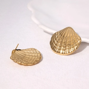 Golden shell stud earrings in stainless steel displayed on a white ceramic plate