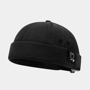 Close-up of black docker hat featuring a woven heart logo label and premium fabric texture