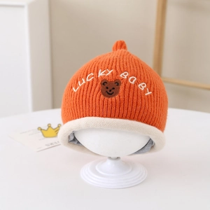 Détail du bonnet tricoté orange pour bébé avec texte Lucky Baby et écusson ours