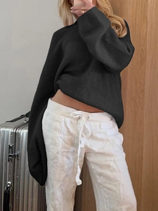 Detail view of a loose black knitted sweater with long sleeves on a model in a room