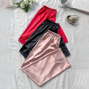 Three pairs of satin lounge pants in red black and pink on a white fabric background