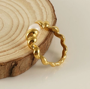 Close-up of golden spiral stainless steel ring with white pearl on a wood base