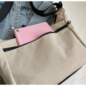 Detail of the large capacity tote bag showing the front zipper pocket with a tablet