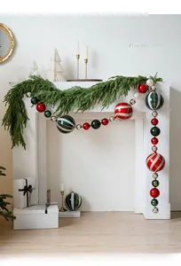 Festive 15cm painted Christmas ball ornaments hung on a mantle with pine and candles