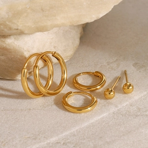 Three-pair set of polished gold stainless steel hoop and ball stud earrings on stone
