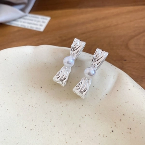 Dettaglio di orecchini a perno con perla argentata su vassoio in ceramica e fondo in legno