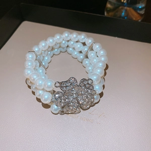 Detailed macro of a triple-row pearl bracelet featuring a sparkling crystal clover clasp