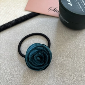 Detail of dark green velvet rose hair tie on a textured surface with soft lighting