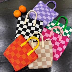 Flat lay of knit checkerboard tote bags in six colors on a dark wood background