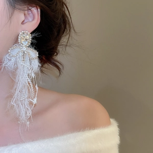 Close-up of elegant bow earrings with long white feather tassels and crystal studs