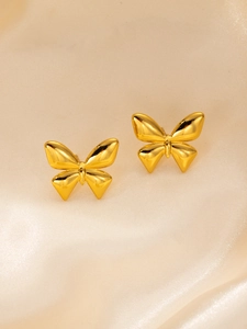 Macro detail of high-polish gold butterfly stud earrings on soft silk fabric