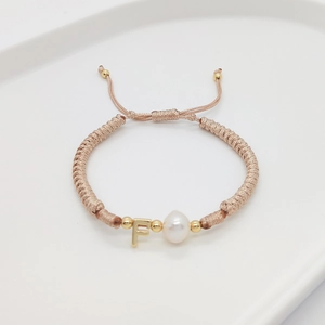 Detail of hand-woven light pink rope bracelet with golden letter F charm and pearl