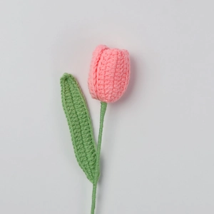 Detailansicht einer handgehäkelten rosa Tulpe mit grünem Strickblatt auf weißem Hintergrund
