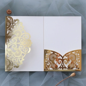 Detail of white laser-cut lace wedding invitation with gold foil accents on blue tulle