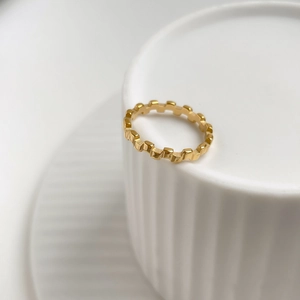 Golden geometric textured ring displayed on edge of white ceramic dish detail