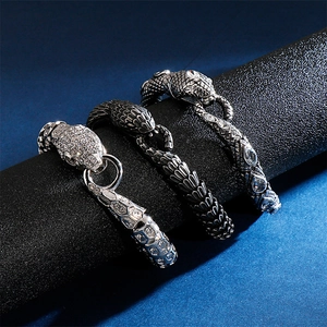Three men's stainless steel snake bracelets with crystals on a black display stand