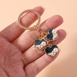 Close-up of gold heart keychain with black enamel and white pearls on beige background