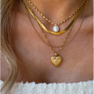 Colliers dorés superposés avec perle et pendentif cœur sur le cou d'un modèle