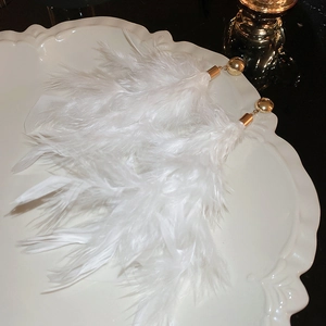 Detailed close-up of white feather tassel earrings with gold studs on a ceramic plate