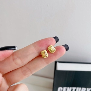 Detailed close-up of rectangular geometric stud earrings with yellow enamel and clear zircon