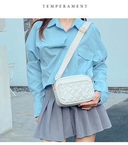 Detail of a white quilted crossbody bag featuring a wide adjustable strap and zipper