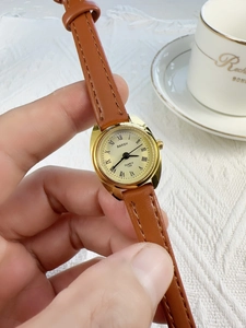 Detailed close-up of a women's quartz watch with a gold case and brown leather strap