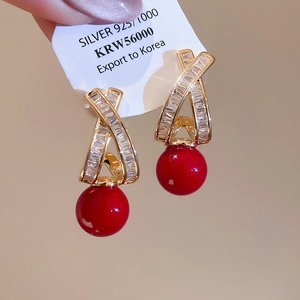 Macro detail of gold-plated cross stud earrings with red beads and 925 silver tag