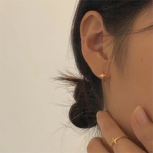 Detail showing minimalist gold star stud earrings and matching open ring on a model