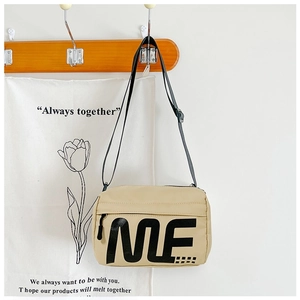 Détail du sac bandoulière en nylon beige avec imprimé lettres ME et sangle ajustable