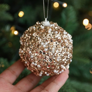 Champagne gold Christmas ball with sequins and pearls held against a festive tree