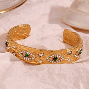 Macro shot of gold evil eye open cuff bracelet with green malachite and zircon detail