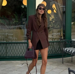 Street style shot of a dark brown slim-fit blazer paired with a black skirt and handbag