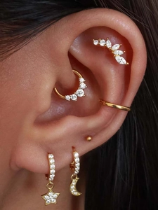 Macro detail of gold star and moon stud earrings with white zircons on ear lobe