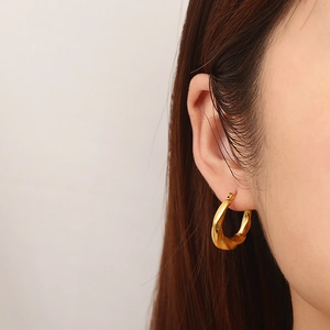 Close-up of golden twisted hoop earrings in titanium steel worn by a model