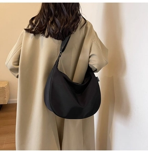 Detail of a large black waterproof Oxford crescent bag worn crossbody with casual trench coat