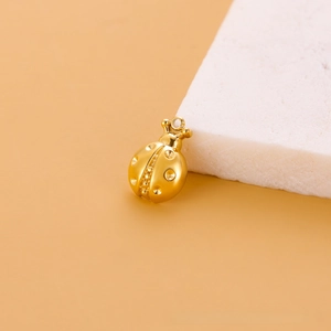 Détail d'un pendentif coccinelle dorée montrant la texture pointillée et l'anneau en métal